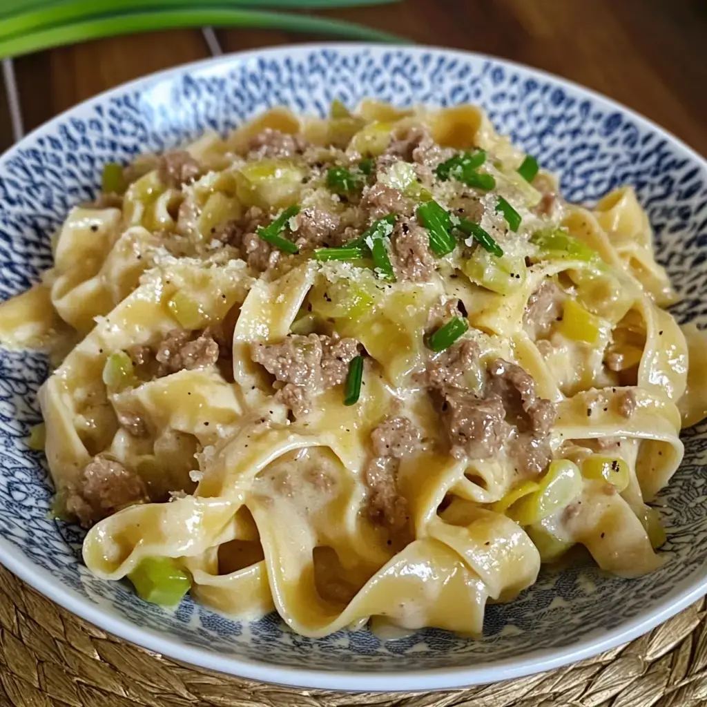 Une assiette de tagliatelles dans une sauce crémeuse, garnie de viande hachée, poireaux, ciboulette et parmesan.
