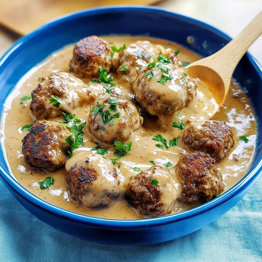 Un bol de boulettes avec une sauce crémeuse, décoré avec du persil frais.