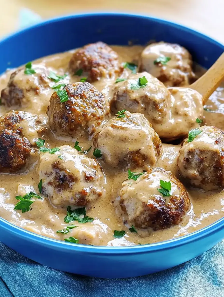 Un bol de boulettes de viande dans une sauce crémeuse, garnies de persil frais.