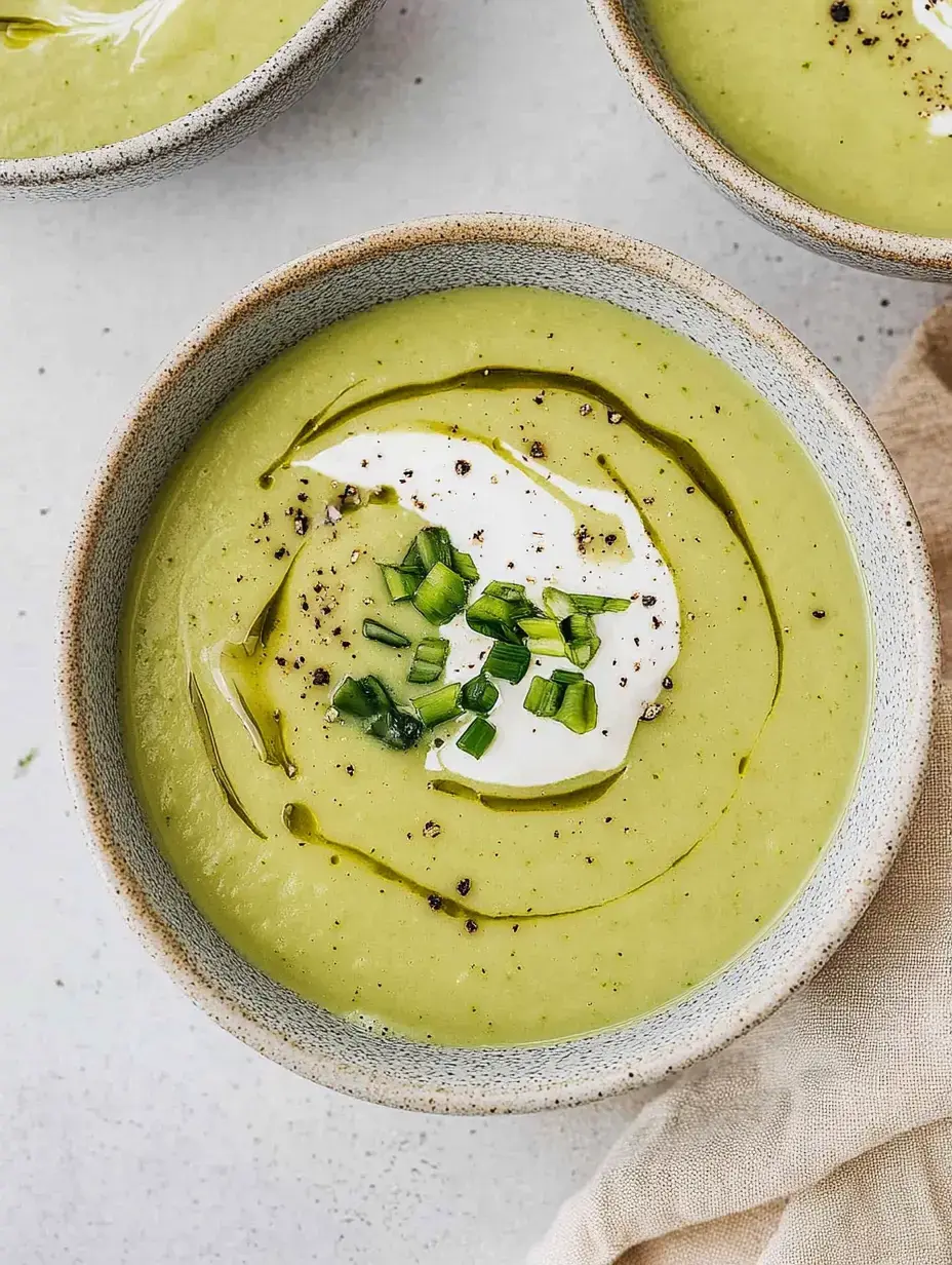 Un bol de soupe verte crémeuse, garnie de crème fraîche, de brins de ciboulette et d'un filet d'huile d'olive.