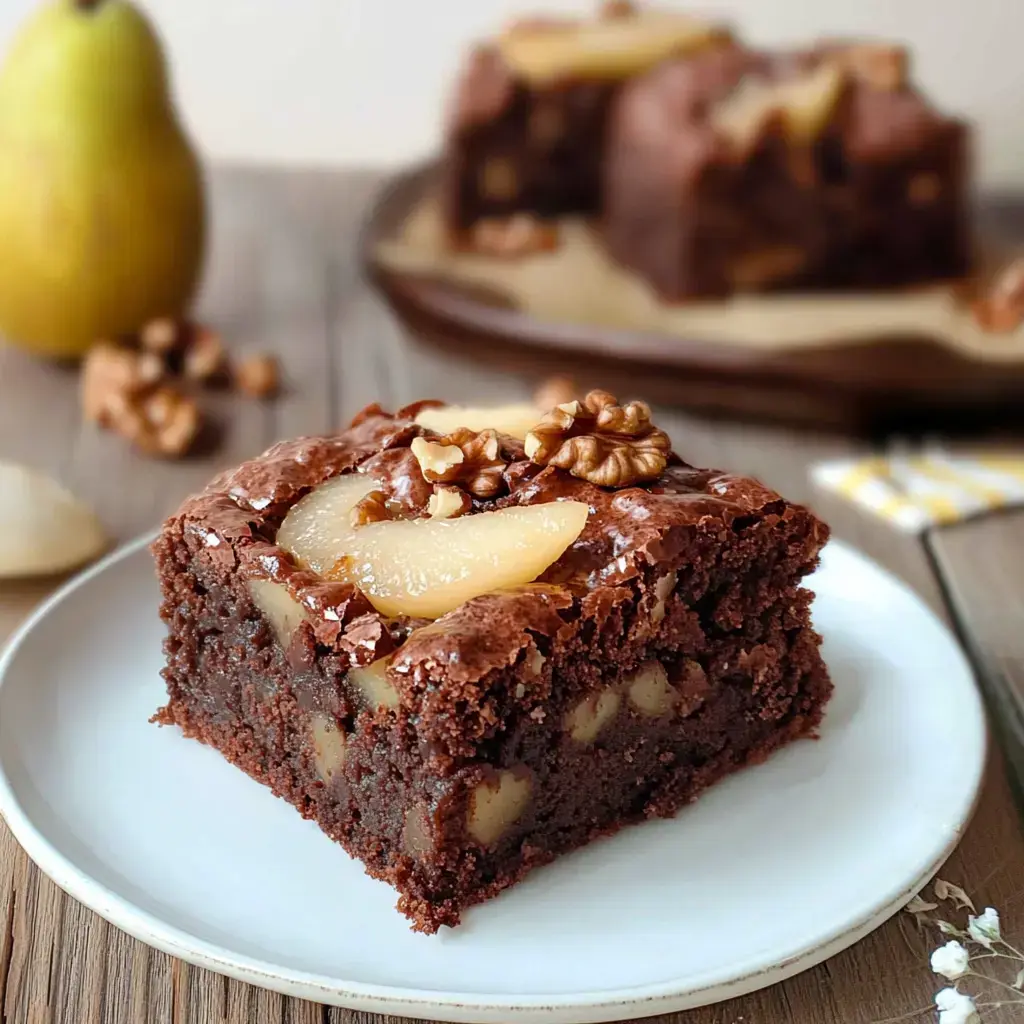 Un morceau de gâteau au chocolat avec des noix et des tranches de poire sur une assiette blanche.