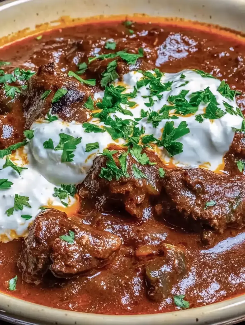 Un plat savoureux avec de la viande juteuse dans une sauce épicée, garni de coriandre fraîche et d'une touche de yaourt.