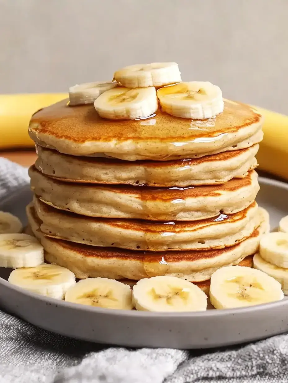 Une pile de crêpes avec des tranches de banane et du sirop sur une assiette.