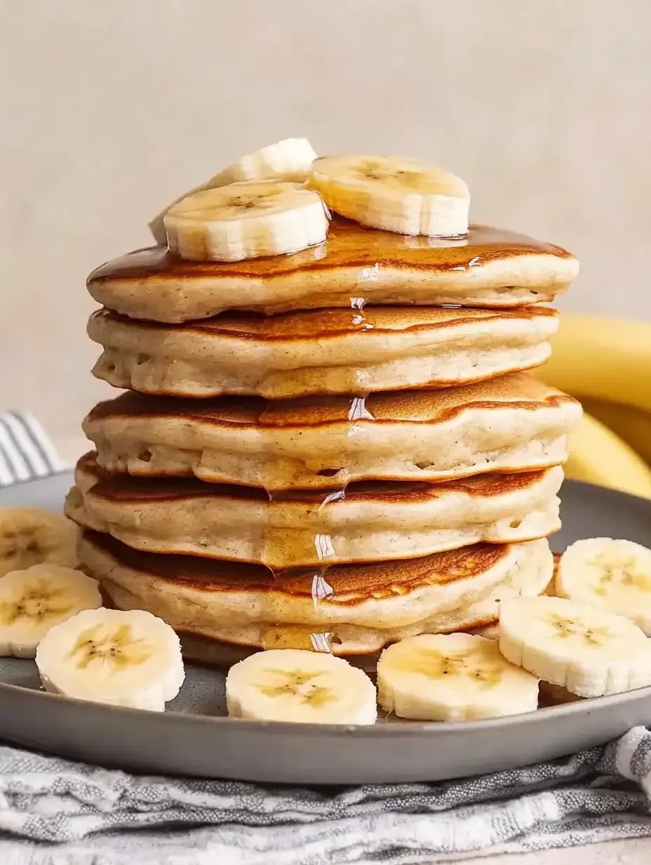 Une pile de crêpes avec des tranches de banane et du sirop, servies sur une assiette grise.