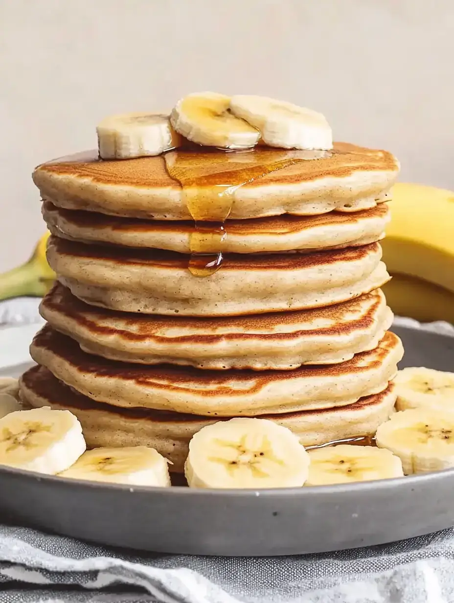 Une pile de crêpes avec des tranches de banane et du miel sur une assiette.