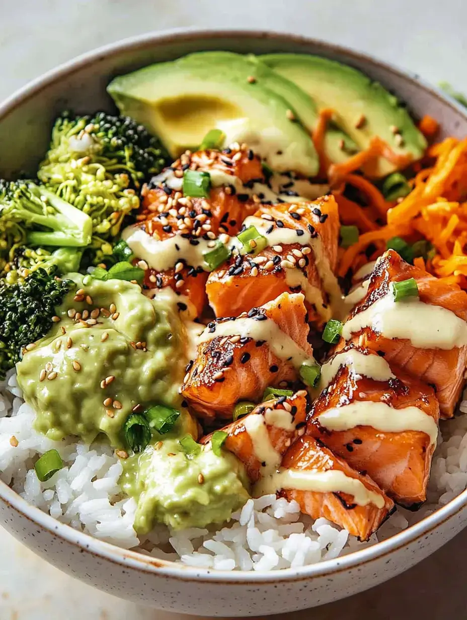 Un bol contenant du riz, saumon grillé, brocoli, tranches d'avocat, carottes râpées, guacamole et sauce crémeuse, garni de sésame et oignons verts.
