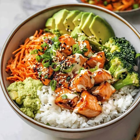 Un bol avec du riz, laxs dorés, carottes, brocolis, avocat, sésame et une sauce crémeuse.