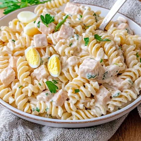 Une assiette de délicieuses pâtes fusilli dans une sauce crémeuse, garnies de petits morceaux de poulet, de persil frais et d'œufs durs coupés en deux.