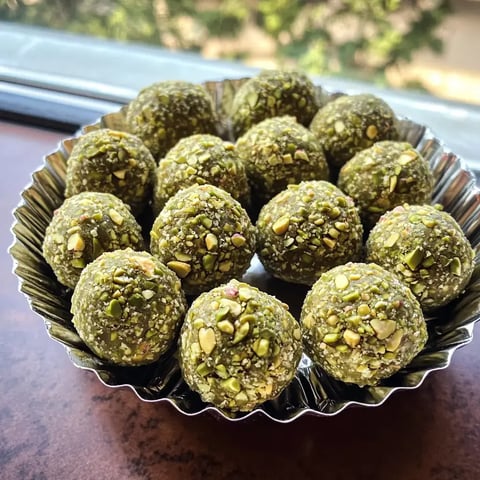 Un bol argenté rempli de petites boules vertes saupoudrées de pistaches hachées.