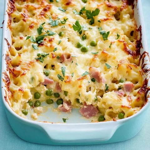 Un gratin de pâtes avec jambon, petits pois et une couche dorée de fromage, décoré de persil frais.