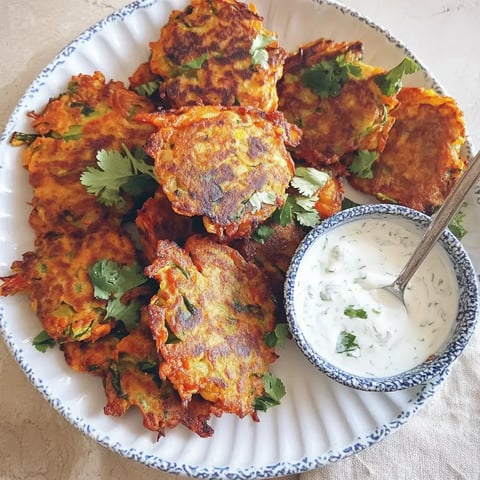 Une assiette de beignets végétariens croustillants, garnis de coriandre, à côté d'un bol de sauce au yaourt.