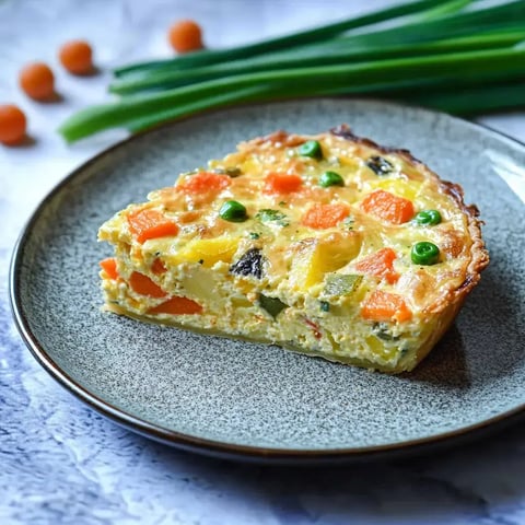 Une part de quiche aux légumes posée sur une assiette grise, décorée avec des morceaux de légumes colorés.