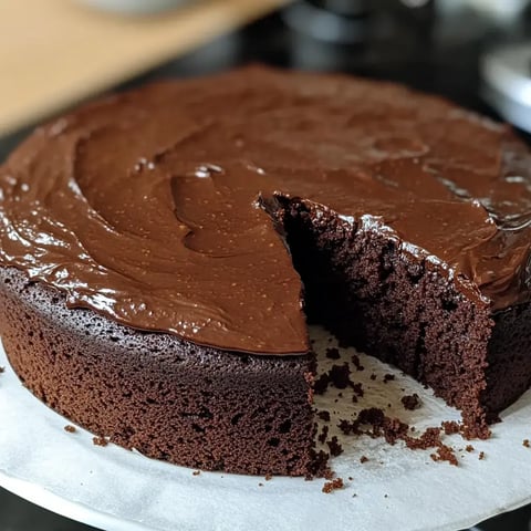 Un gâteau au chocolat moelleux avec glaçage lisse, dont une part a été coupée.
