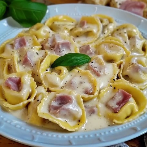 Un bol de tortellini dans une sauce crémeuse, garni d'une feuille de basilic frais.
