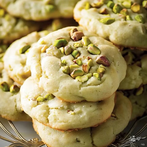 Un tas de biscuits moelleux aux pistaches disposés sur un plateau doré.