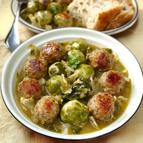 Une assiette avec des boulettes de viande, des choux de Bruxelles et du bouillon de légumes, servie avec du pain frais.